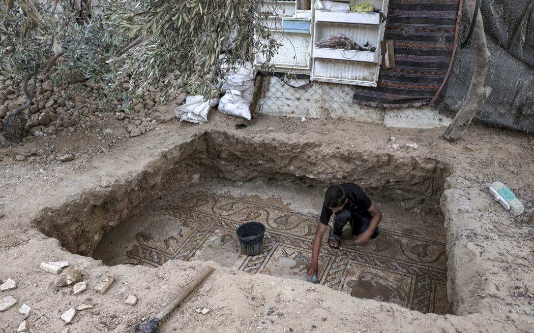 The son of Palestinian farmer Salman al-Nabahin uses a sponge to uncover Byzantine mosaics dating from the fifth to seventh centuries after being discovered by his father while working on his land in the central Gaza Strip on 18 September, 2022.