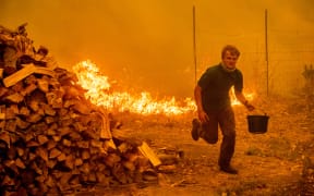 Alex Schenck, 15, carries a water bucket while fighting to save his home as the Ranch Fire tears down New Long Valley Rd in California.