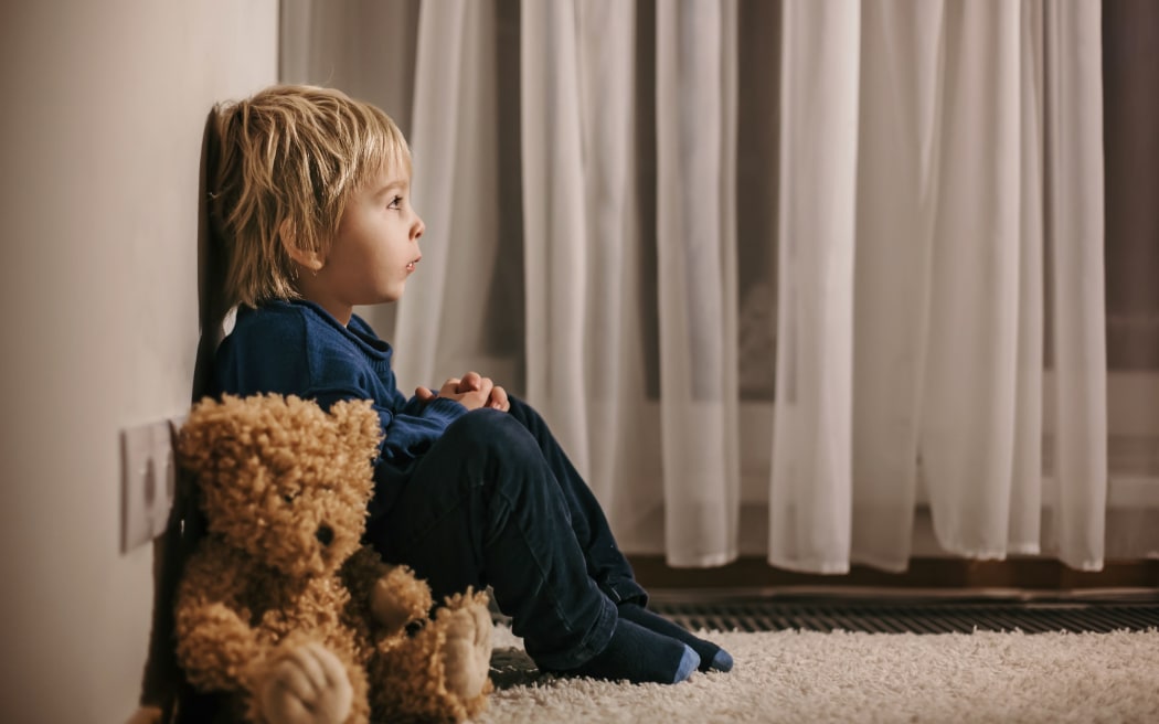 Sad child sitting in corner with teddy bear.