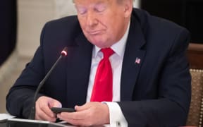 US President Donald Trump uses his cellphone as he holds a roundtable discussion with Governors about the economic reopening of closures due to COVID-19, known as coronavirus, in the State Dining Room of the White House in Washington, DC, June 18, 2020. (Photo by SAUL LOEB / AFP)