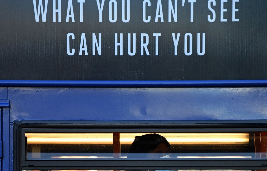 A woman wearing a face mask or covering due to the COVID-19 pandemic, sits beneath a sign reading "What you can't see, Can hurt you", as she travels by bus in Manchester.