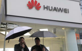 FILE - In this Thursday, March 7, 2019 file photo, two men use their mobile phones outside a Huawei retail shop in Shenzhen, China's Guangdong province.