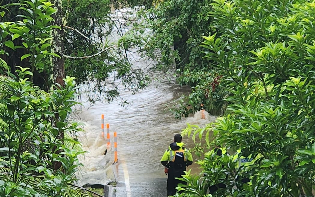 Police inspect a section of Falls Road near the Mahurangi River where a person and their vehicle is believed to have been swept into the river