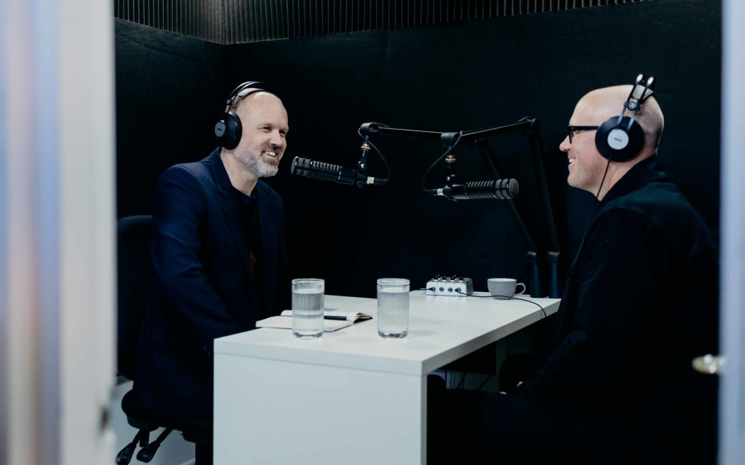 Reverend Frank Ritchie and Garth Bray sitting across a desk in a small radio studio, chatting.