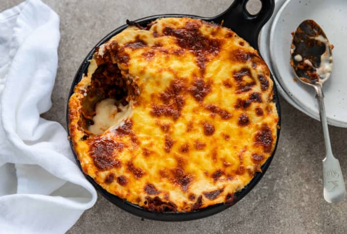 A round dish of lamb lasagne covered with a baked cheese topping.