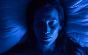 A woman lies with closed eyes on a pillow in blue light.
