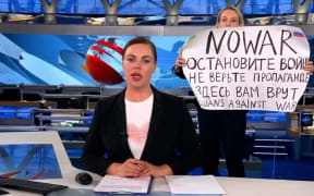 An unidentified woman runs out behind the back of the news anchor woman during on-air news on Monday March 14, 2022 evening news program at the Russia state television Channel One.
