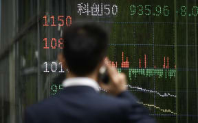 A man looks at a screen showing Chinese stock market movements as he uses his mobile phone in Beijing on April 7, 2025. Asian equities collapsed on a black Monday on April 7 for markets after China hammered the United States with its own hefty tariffs, ramping up a trade war many fear could spark a recession. (Photo by WANG Zhao / AFP)