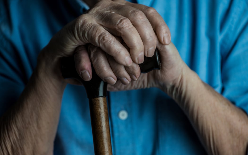 Close-up view of senior man hands leaning on a cane while sitting