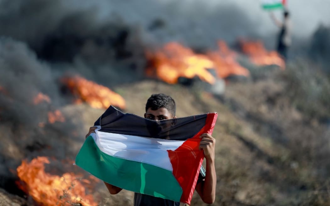 A Palestinian holds a flag during a protest against Israeli army raid in Jenin, along Israel-Gaza border fence east of Gaza City July 3, 2023. Israel has stepped up operations in the northern West Bank, home to Jenin city and its adjacent refugee camp, a stronghold of Palestinian armed groups where there has been a spate of attacks on Israelis as well as attacks by Jewish settlers on Palestinian communities. 
 (Photo by Majdi Fathi/NurPhoto) (Photo by MAJDI FATHI / NurPhoto / NurPhoto via AFP)