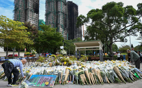 Mourners lay flowers as they pay their respects for victims at a makeshift memorial outside the Wang Fuk Court apartment blocks in the aftermath of the deadly November 26 fire in Hong Kong's Tai Po district on December 1, 2025. Police as well as Hong Kong's anti-corruption watchdog have launched investigations into the blaze that have killed at least 146 people, but a petition calling for greater accountability and demanding an independent probe was swiftly shut down as an organiser was reportedly arrested for sedition. (Photo by Peter PARKS / AFP)