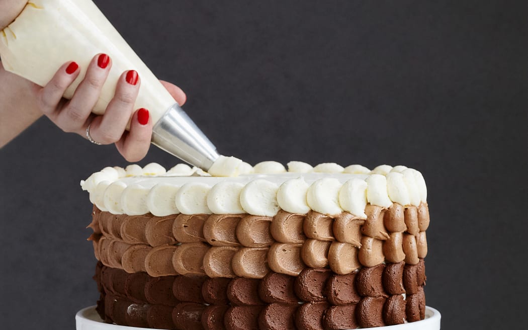 A person's hands seen piping icing on a cake.