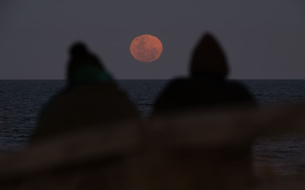 People look at the super blue moon as it rises above the sea in New Brighton, Christchurch, New Zealand on August 31, 2023. The blue moon is a term used to describe the second full moon in a single calendar month. But this year's blue moon also coincides with a supermoon, which is when the moon is at its closest point to Earth in its elliptical orbit, appearing larger and brighter than usual. It’s exceptionally close in Moon miles from Earth (222,043 miles). The last super blue moon occurred in 2009, and the next won’t be until 2037 according to NASA. (Photo by Sanka Vidanagama/NurPhoto) (Photo by SANKA VIDANAGAMA / NurPhoto / NurPhoto via AFP)