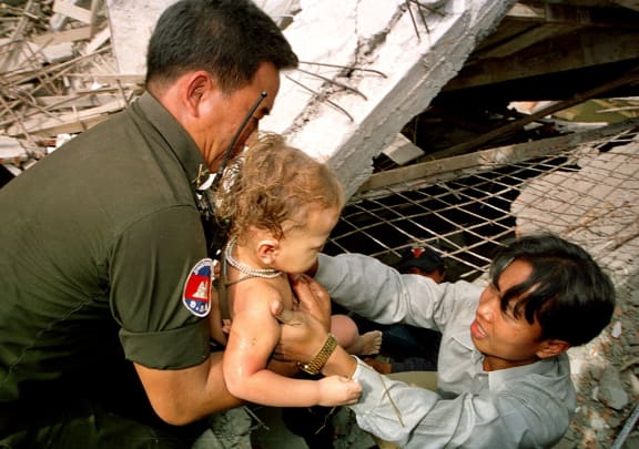 A Cambodian rescuer helped by a policeman, removes a baby from the wreckage as he survived the collapse of a building in Phnom Penh.