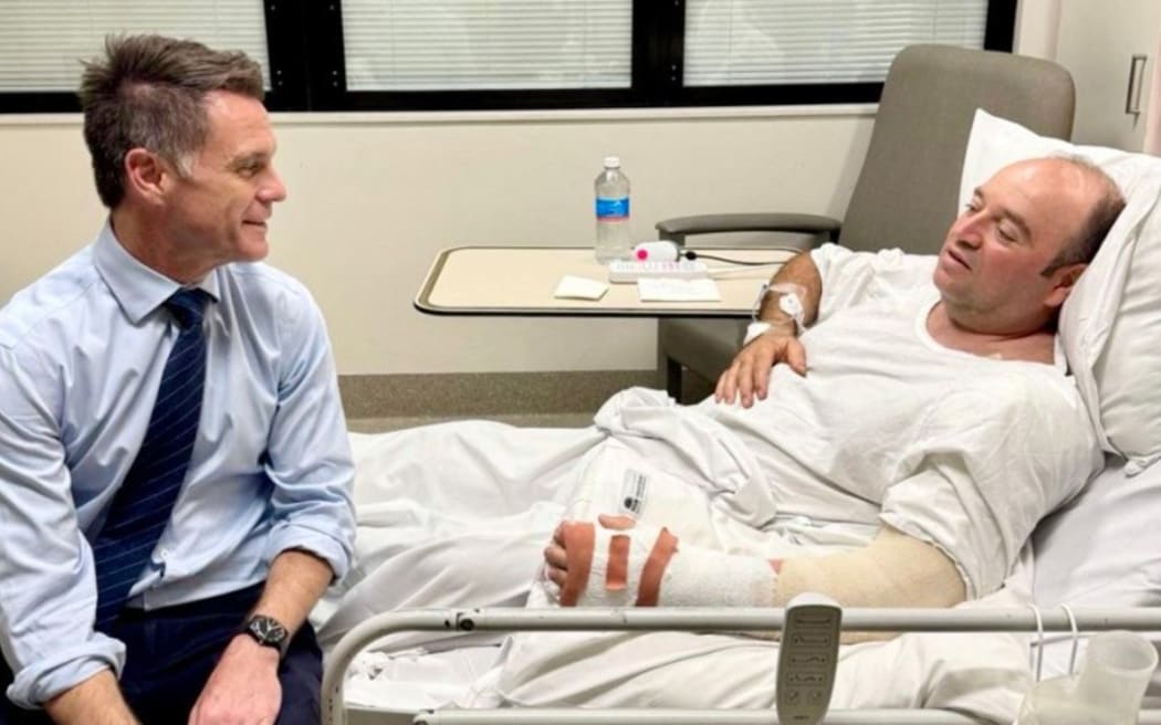 This handout photo taken and received from the NSW Premier's Department on 15 December 2025 shows New South Wales Premier Chris Minns (L) talking with Ahmed Al Ahmed, the man who tackled and disarmed one of the Bondi Beach attackers, at St George Hospital in Sydney. Australia's leaders agreed on December 15 to tougher gun laws after the country's worst mass shooting in almost three decades saw a father and son open fire on a Jewish festival at Bondi Beach, killing 15 people including a child.