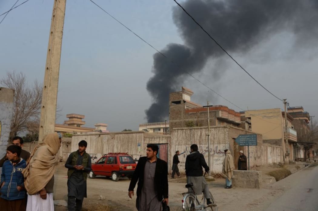 Afghan civilians gather on a street next to a plume of smoke coming from the area around an office of the British charity Save the Children.
