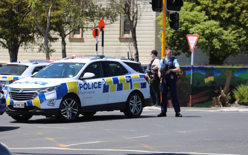 Lights are out at Birkenhead Ave intersection with Onewa Road and traffic is being manually directed by a person in a high-vis vest while armed police guard a cordon.