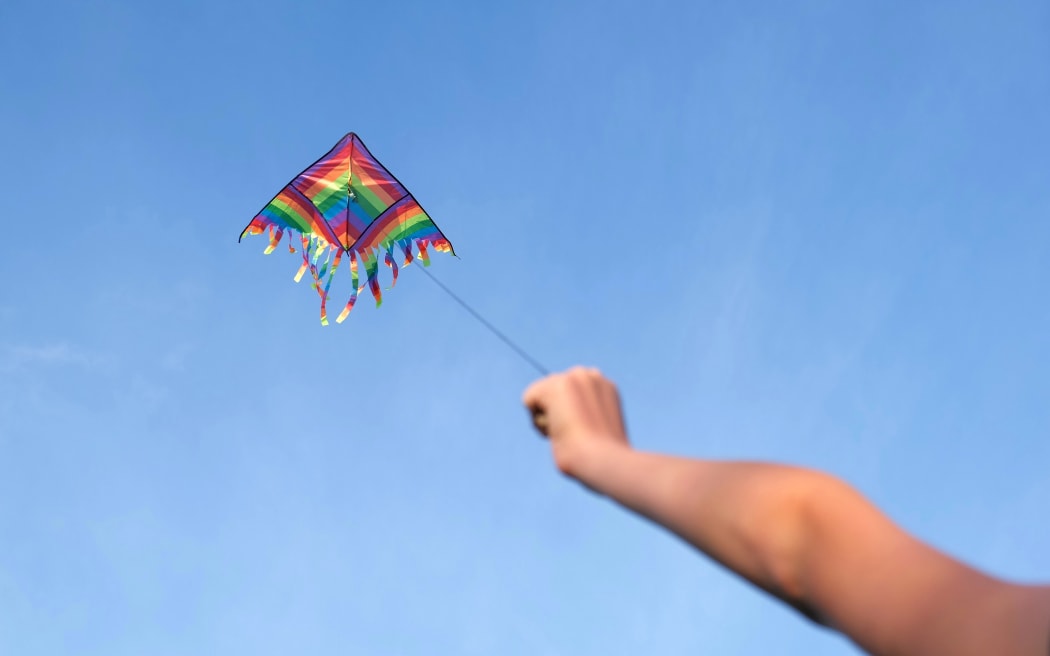 Kite in a blue sky. Happy Teen girl flying Rainbow Delta. Happy growing years moment. Outdoor time spending. Aspirations, target, inspiration concept. Freedom and summer holiday. Childhood dream.