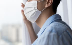 asian young man with face mask stay isolation at home for self quarantine due to an epidemic of COVID-19 and he looks out by windows. Home isolation. Isolating. Isolation. MIQ. Quaranatine