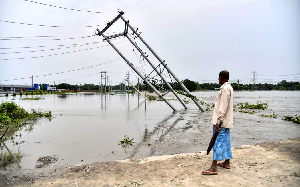 A man looks at overturned electric pillars which were damaged by flood waters in Rangia of Kamrup district, in India's Assam state on 19 June, 2022.