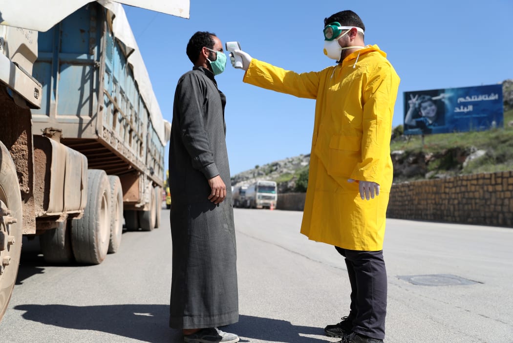 A Syrian civil defence worker in a protective suit measures the temperature of a man at the Bab el-Hawa border crossing with Turkey amid the COVID-19 pandemic on April 14, 2020.