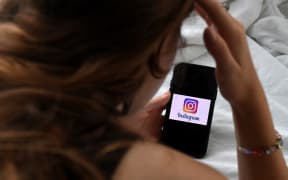 (FILES) In this photo illustration, a person looks at a smart phone with a Instagram logo displayed on the screen, on August 17, 2021, in Arlington, Virginia. Meta on September 17, 2024, announced the creation of "Teen Accounts," designed to better protect underage users from the dangers associated with Instagram. The hugely popular photo-sharing app is accused by many experts and authorities of damaging the mental health of its youngest users. (Photo by OLIVIER DOULIERY / AFP)