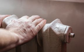 An elderly man warms his hands on the Central heating battery.