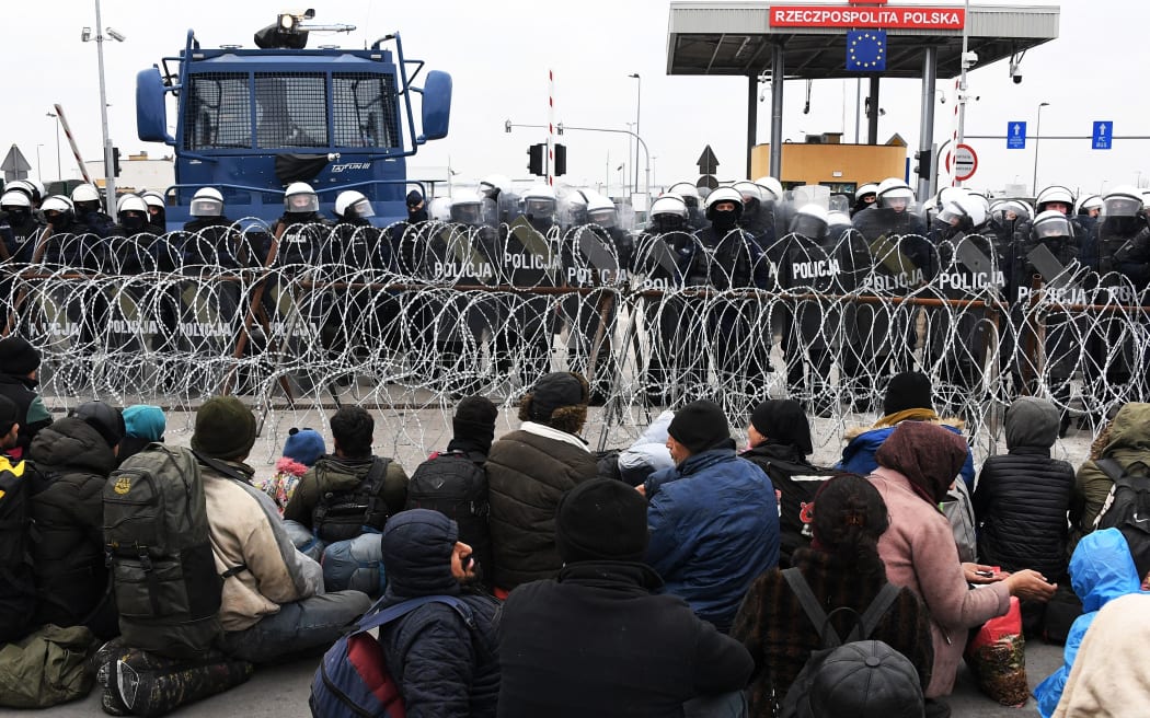 6696060 15.11.2021 Refugees gather at the Bruzgi-Kuznica Bialostocka border crossing as Polish police officers stand guard behind a fence near the Belarusian-Polish border, Belarus.