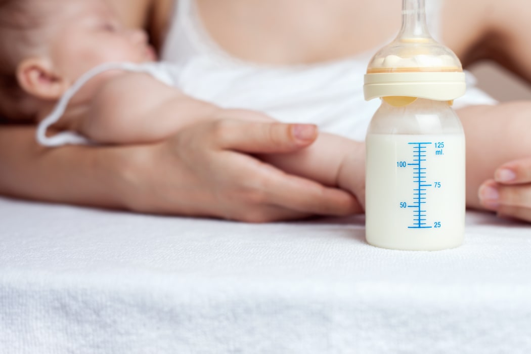 A mother holds a baby next to a bottle of milk.