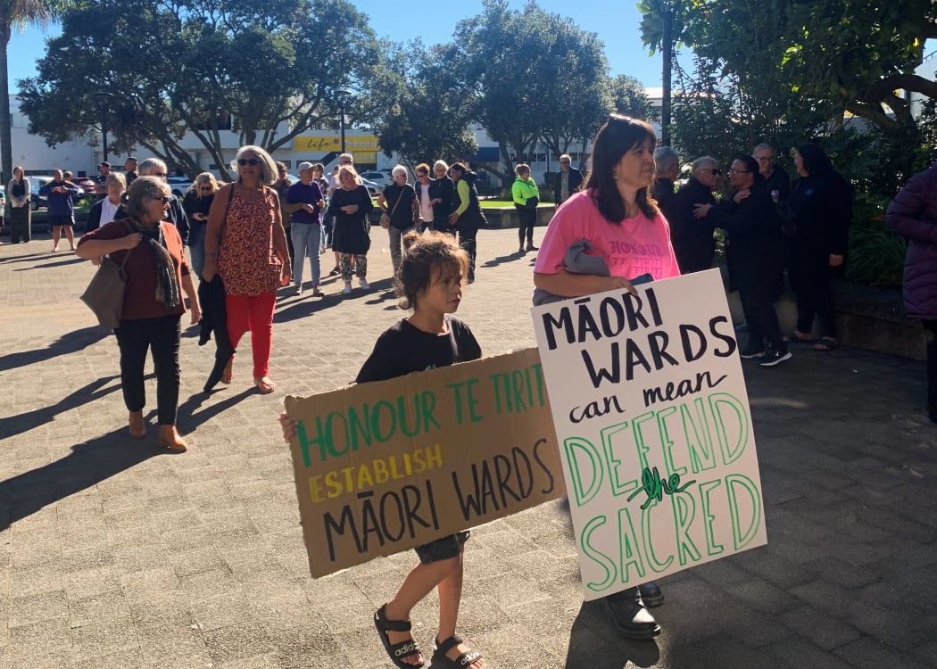 Supporters of Māori wards arrive at council carrying signs indicating what wards could mean for them. The sign “defend the sacred” carried by Lanae Cable refers to the potential development of the Opihi urupa at Whakatāne.