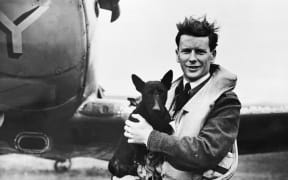 Portrait of Flying Officer John Milne Checketts, after returning from a mission, standing in front of a Spitfire with Alan Deere's dog. Unknown location in England.