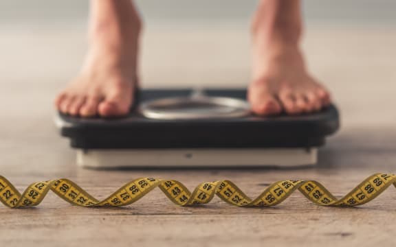 Person standing on weigh scales, tape measure in the foreground.