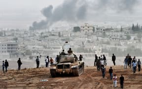 Turkish soldiers on a tank and Kurdish people looking towards Kobane from a hill on the Turkish-Syrian border.