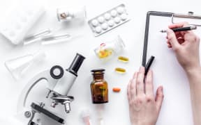 Hand writes on tablet near microscope.