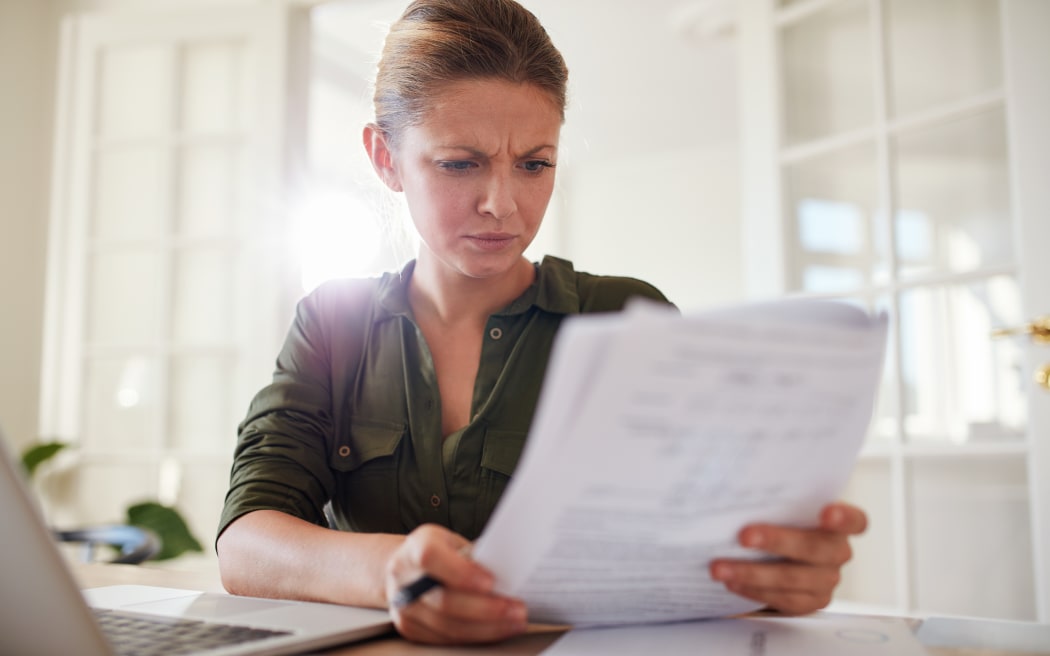 Portrait of a young female with a furrowed brow sitting at a table reading documents.
