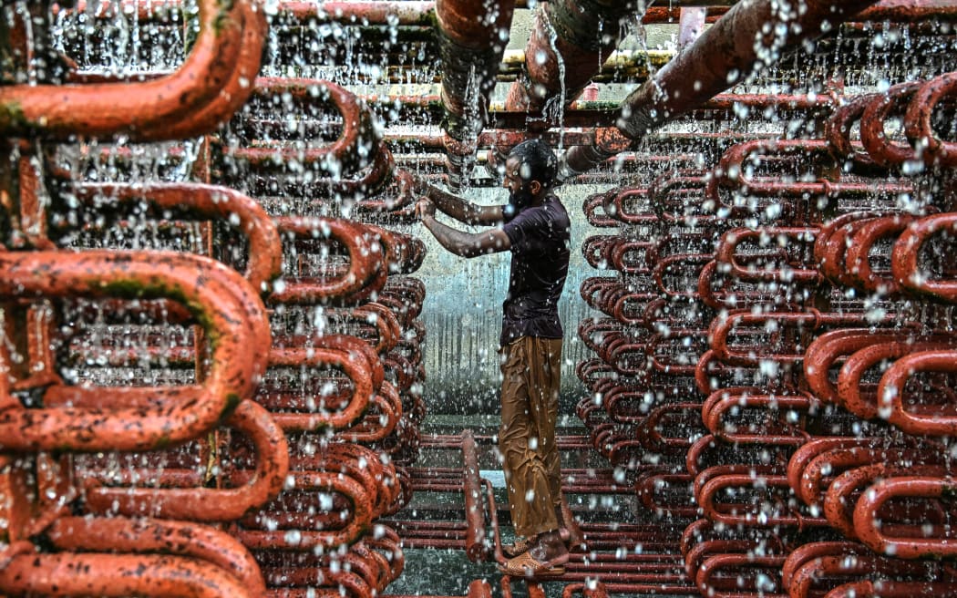 A worker cleans the lines of a cooling tower at an ice factory on a hot summer day in Karachi on May 29, 2025.