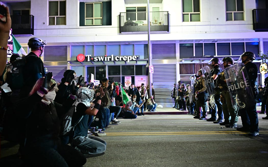 Protesters kneel in the street facing a row of police in riot gear during a protest in response to federal immigration operations in the Little Tokyo neighborhood of downtown Los Angeles, on June 9, 2025. President Donald Trump's administration said on June 9 that it was sending 700 US Marines and thousands more National Guard troops to Los Angeles, sparking a furious response from California's governor over the "deranged" deployment. Protests in Los Angeles, home to a large Latino population, broke out on June 6, triggered by immigration raids that resulted in dozens of arrests of what authorities say are illegal migrants and gang members. (Photo by Frederic J. Brown / AFP)