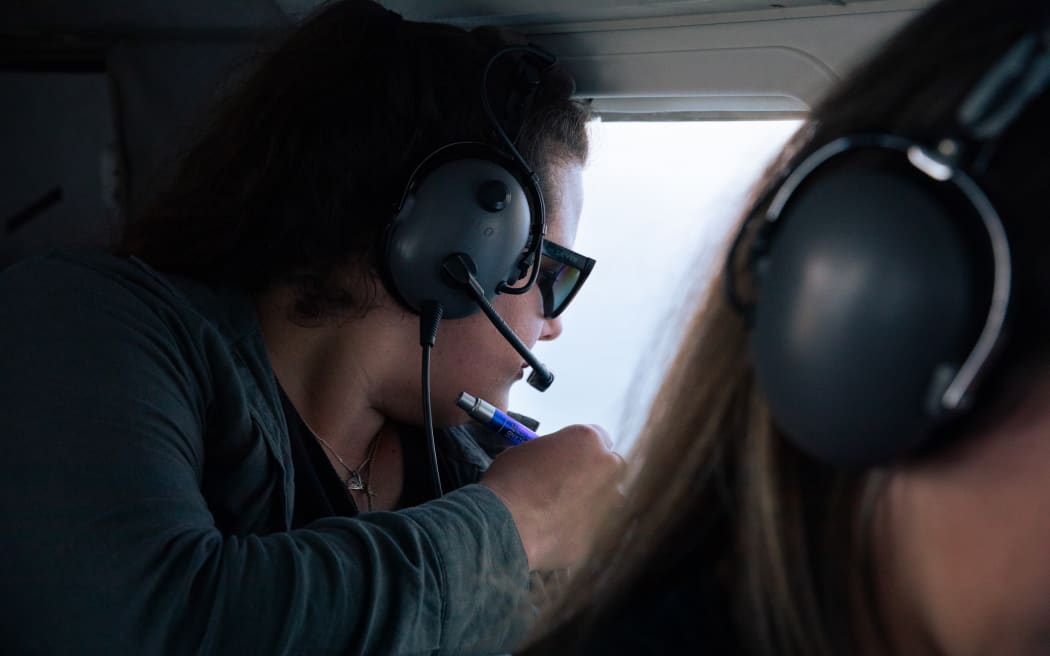 Catherine Meyer holds a pen ready to take notes while looking out a plane window.