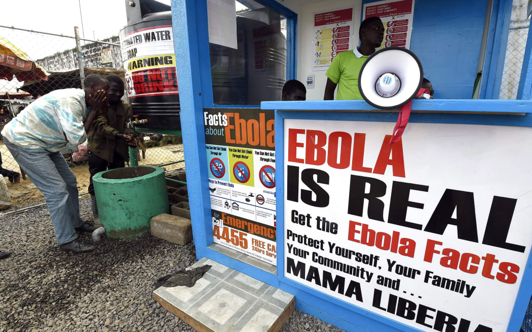 Liberians wash their hands next to an Ebola information and sanitation station.