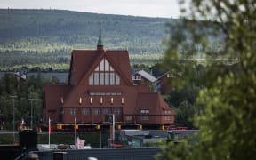 The wooden Kiruna Church is seen in the background as it is being transferred to its new location, in Kiruna, Sweden on August 19, 2025. The church is being moved five kilometers to the new center of Kiruna due to the expansion of the iron ore mine operated by state-owned Swedish mining company LKAB. (Photo by Jonathan NACKSTRAND / AFP)