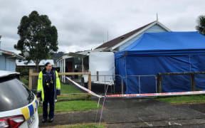 Police are executing a search warrant at a house on Taraire Street in relation to the investigation into the homicide of Linda Woods. At least four officers are guarding the cordoned house and other officers can be seen rummaging through rubbish bins on the property.