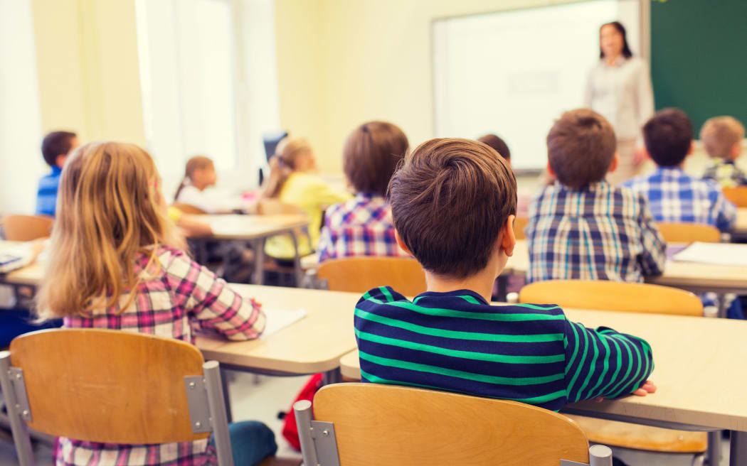 education, elementary school, learning and people concept - group of school kids sitting and listening to teacher in classroom from back