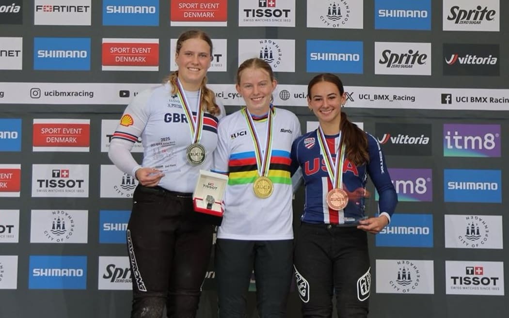Lily Greenough (middle) with her gold medal for winning the 2025 Junior women's BMX Racing World Championship title.