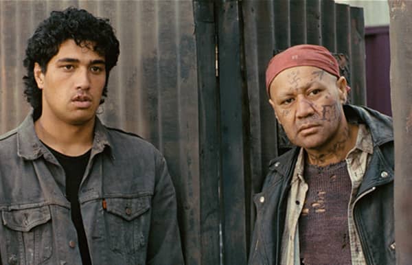 Two young men stand outside a gate looking concerned.