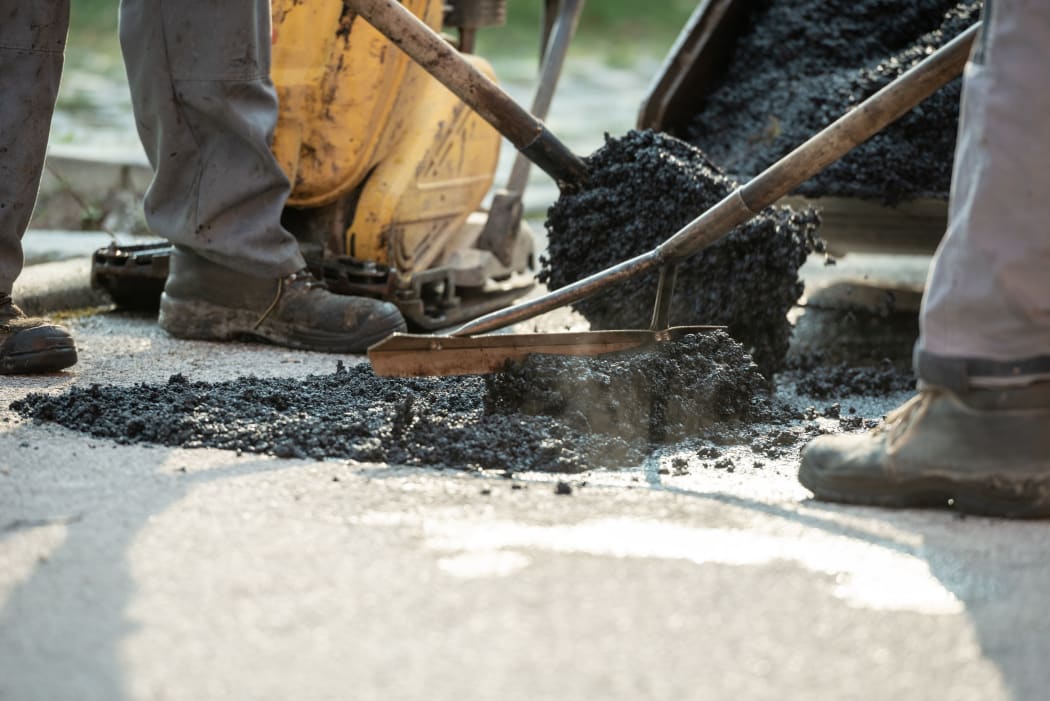 Two construction workers working together to patch a bump in the road with fresh asphalt.