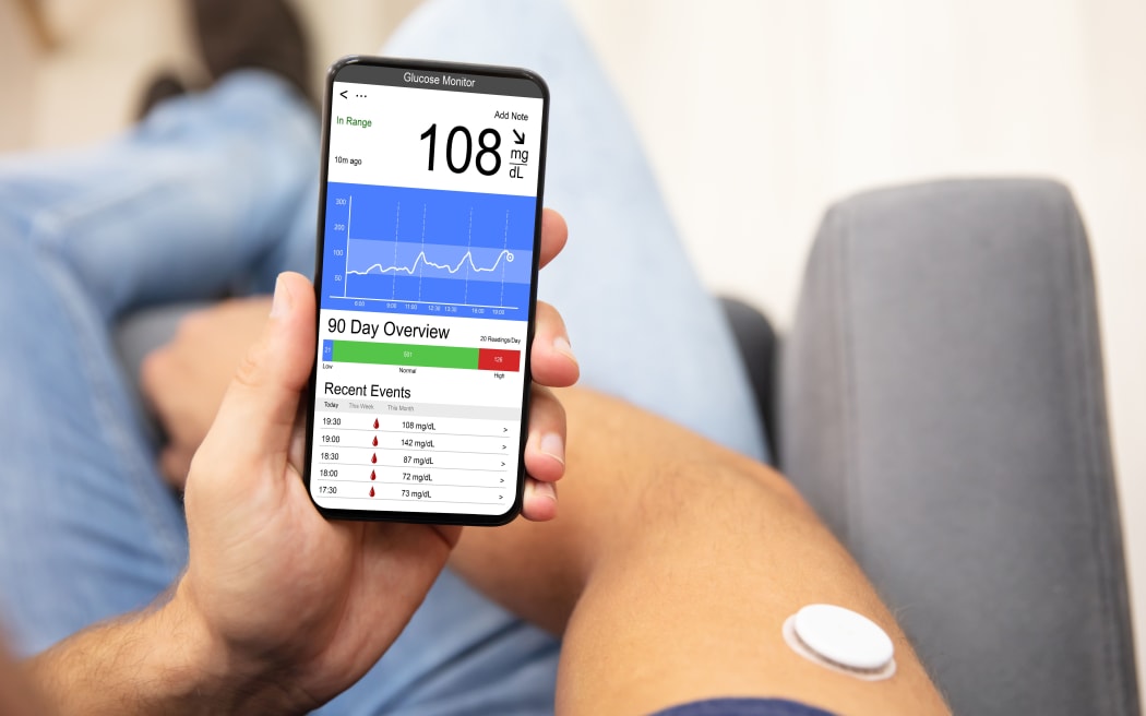 Man Holding Smartphone In Hand With Bad Level Of Blood Sugar On The Screen - Continuous Glucose Monitor for diabetes
