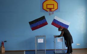 DONETSK OBLAST, UKRAINE - SEPTEMBER 24: A woman hangs flags as people cast their votes in controversial referendums  in Donetsk Oblast, Ukraine on September 24, 2022. Voting will run from Friday to Tuesday in Luhansk, Donetsk, Kherson and Zaporizhzhia, with people asked to decide if they want these regions to become part of Russia. Stringer / Anadolu Agency (Photo by STRINGER / ANADOLU AGENCY / Anadolu Agency via AFP)