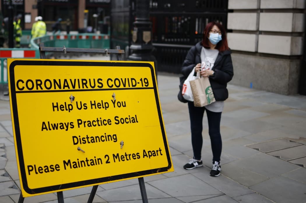 A shopper wearing a facemask stands near a sign promoting social distancing in Haymarket, central London on January 8, 2021, as England entered a third lockdown due to the novel coronavirus Covid-19.