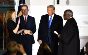 US President Donald Trump watches as Supreme Court Associate Justice Clarence Thomas (R) swears in Judge Amy Coney Barrett as a US Supreme Court Associate Justice, flanked by her husband Jesse M. Barrett, during a ceremony on the South Lawn of the White House October 26, 2020.