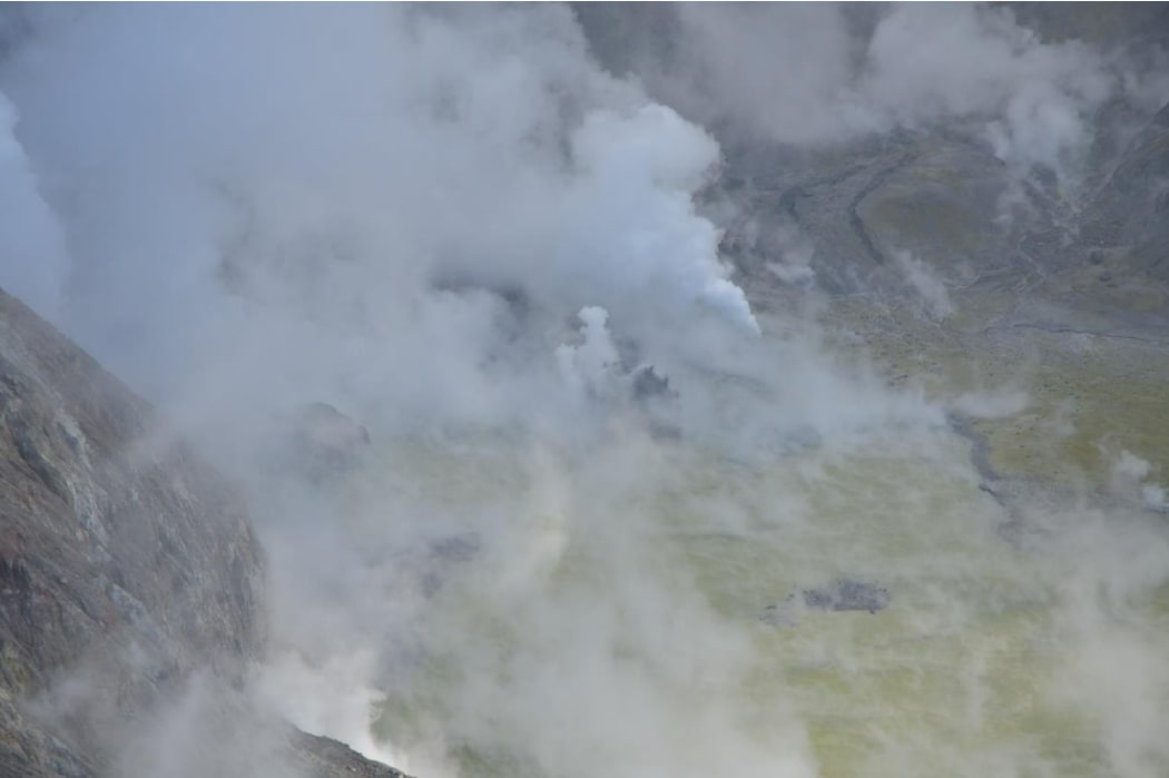 View into crater of Whakaari / White Island on 24 May, 2024, showing greysering, ejecting steam and dark material.